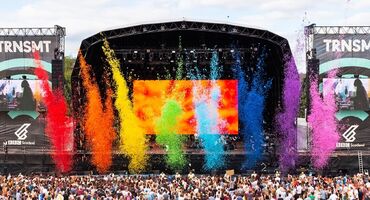Colourful confetti in rainbow colours is fired towards a large crowd in front of an outdoor stage.