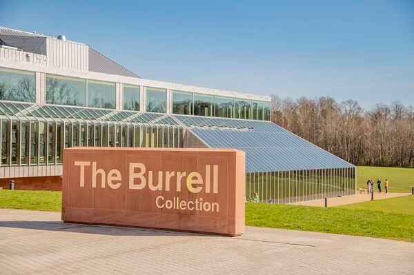 The exterior of The Burrell Collection in Glasgow. A sign reading 'The Burrell Collection' stands in front of the museum with trees behind.
