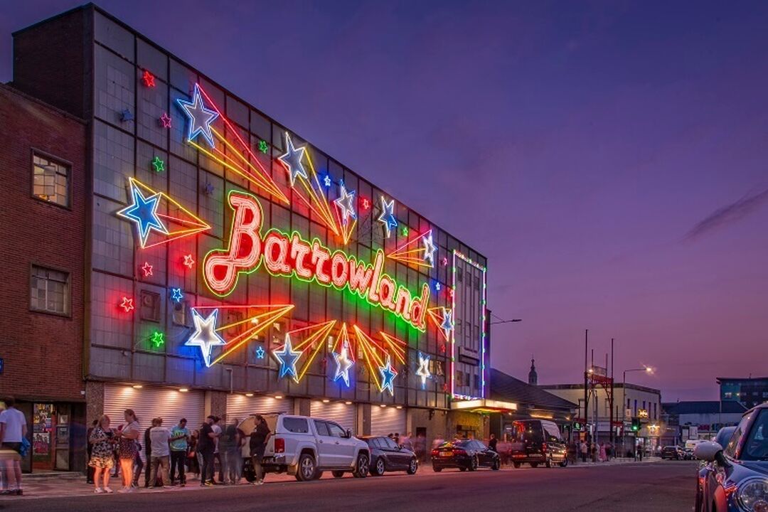 The famous neon sign that reads Barrowlands with neon shooting stars. The Barrowland venue sits against a purple/pink sky at dusk.